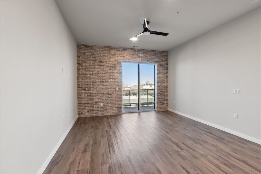 Spare room with ceiling fan, brick wall, baseboards, and wood finished floors