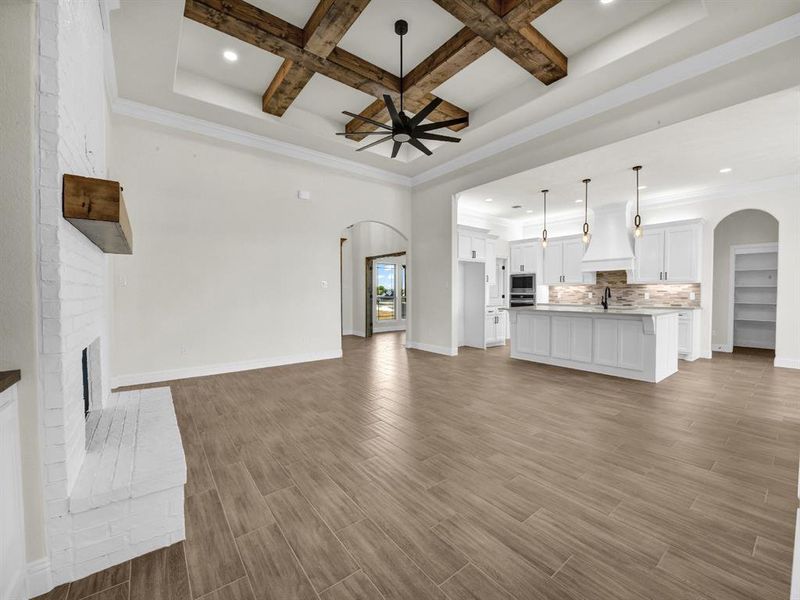 Unfurnished living room with arched walkways, ceiling fan, coffered ceiling, and light wood finished floors Unfurnished living room with arched walkways, ceiling fan, coffered ceiling, and light wood finished floors