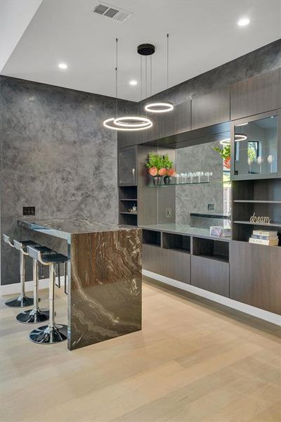 Bar with modern cabinets, decorative light fixtures, and dark stone countertops Bar with modern cabinets, decorative light fixtures, and dark stone countertops