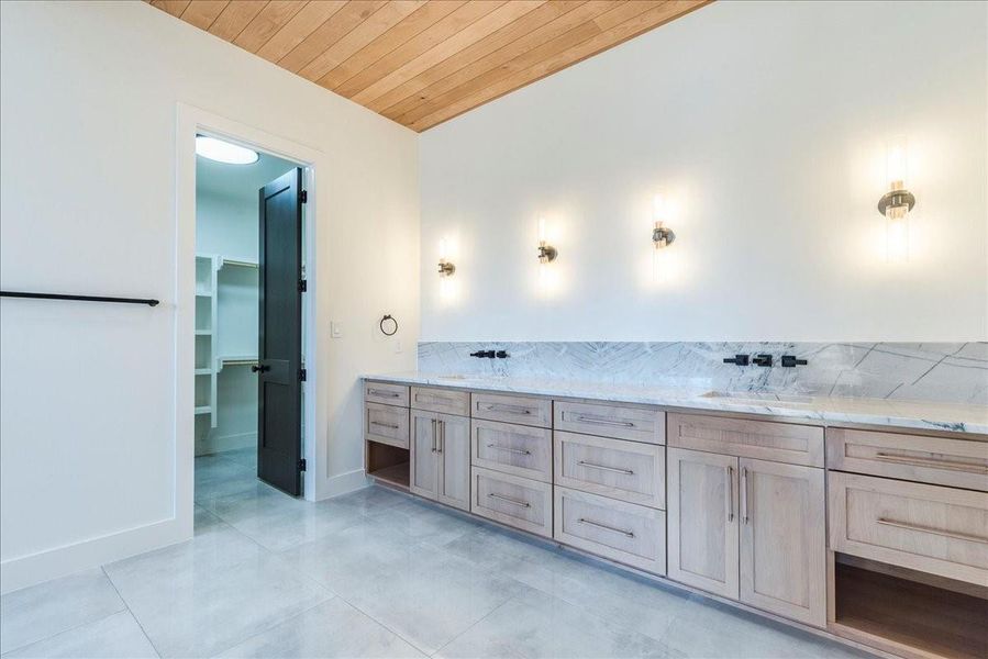 The luxurious primary bath boasts 4' x 3' porcelain tile flooring, paired with light wood cabinetry and sleek black accents.