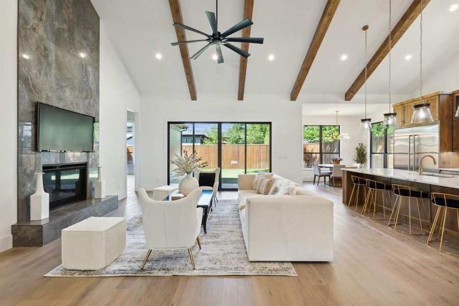 Living room with light wood-type flooring, beamed ceiling, high vaulted ceiling, a tiled fireplace, and ceiling fan