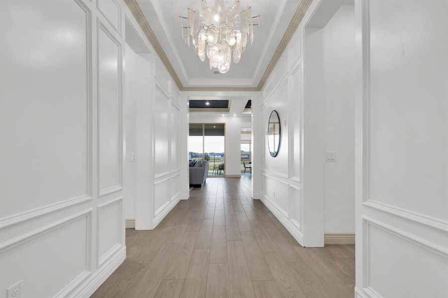 Hall with a decorative wall, light wood-type flooring, a chandelier, and a tray ceiling