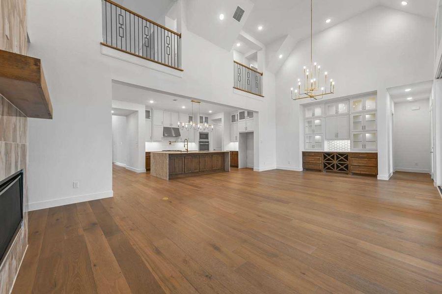 Unfurnished living room featuring sink, a towering ceiling, a fireplace, hardwood / wood-style floors, and an inviting chandelier