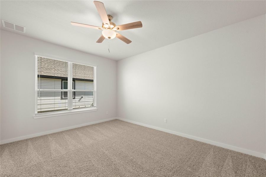 Well-lit room with ample space, featuring soft carpeting and a ceiling fan for comfort.