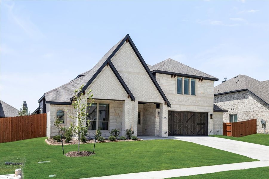 Two-story home with light stone exterior, dark trim, two-car garage, and manicured front lawn