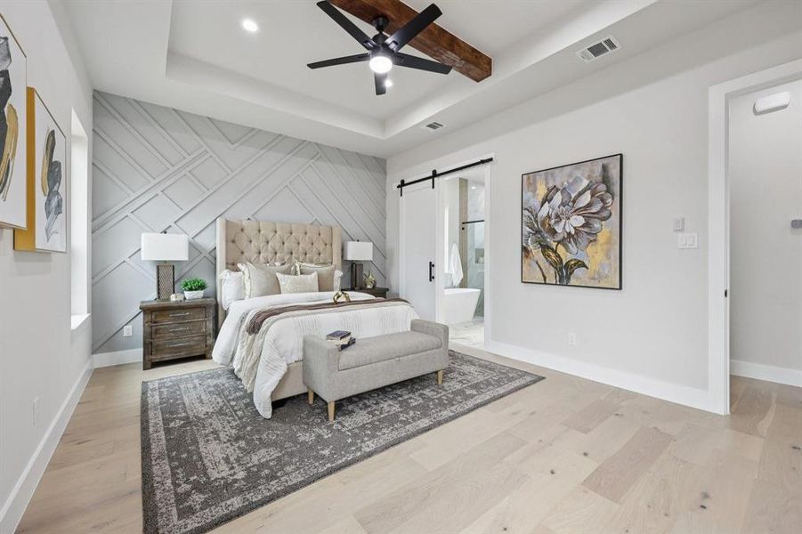 This bedroom features light wood flooring, a decorative accent wall, and a tray ceiling with exposed wooden beams