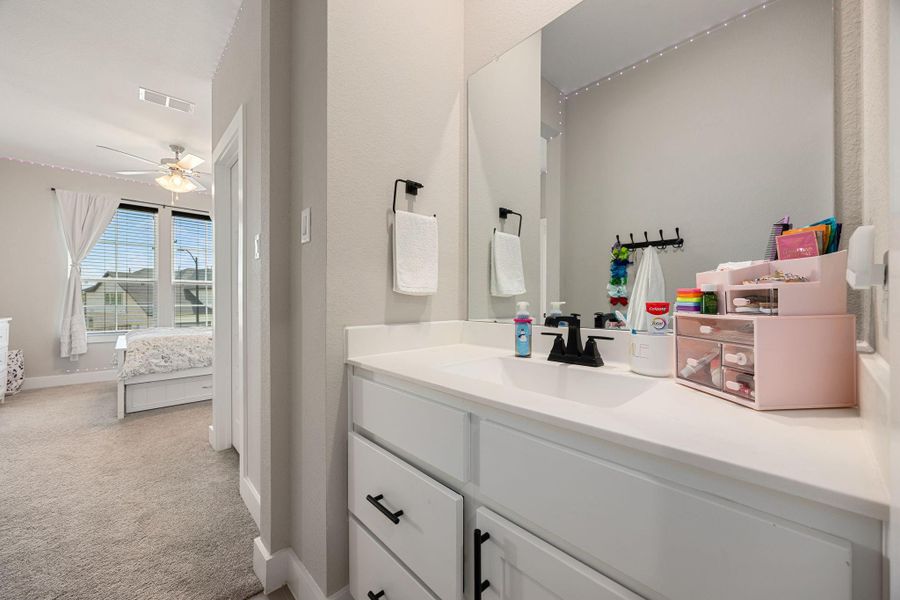 This Jack-and-Jill style bathroom features a spacious vanity with dual sinks, sleek black hardware, and ample storage. Neutral tones and a large mirror enhance the bright, open feel, while direct access to the adjoining bedroom makes it both functional and convenient.