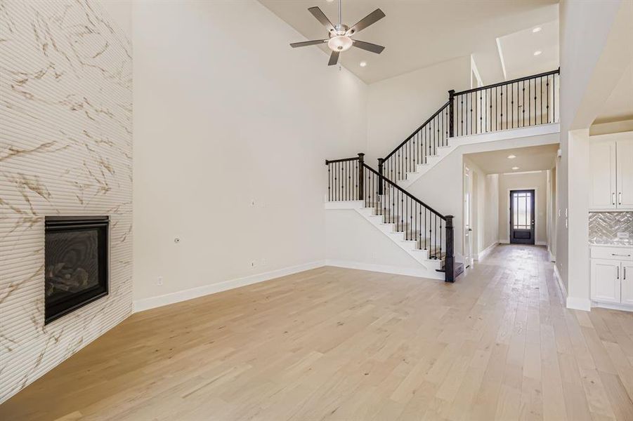 Unfurnished living room featuring a tile fireplace, light wood finished floors, recessed lighting, a high ceiling, and stairway Unfurnished living room featuring a tile fireplace, light wood finished floors, recessed lighting, a high ceiling, and stairway