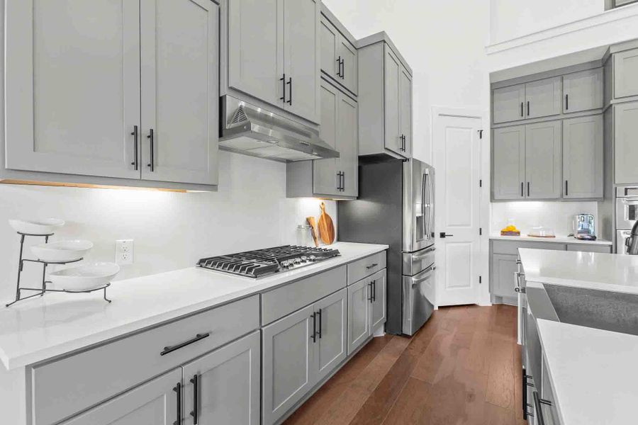 Modern kitchen featuring light gray cabinetry, stainless steel appliances, a gas cooktop, white countertops, and wood-finish flooring