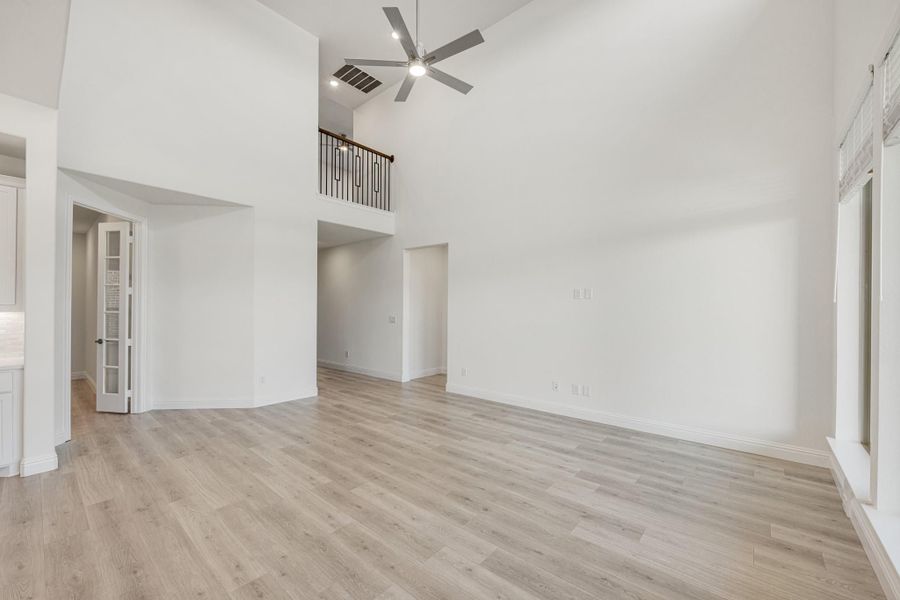 Open living area with two-story ceiling, ceiling fan, light wood floors, and upper balcony overlook Open living area with two-story ceiling, ceiling fan, light wood floors, and upper balcony overlook