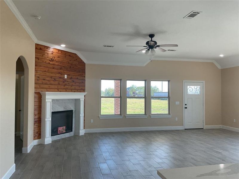 Unfurnished living room featuring crown molding, light wood-style flooring, a fireplace, a ceiling fan, and arched walkways Unfurnished living room featuring crown molding, light wood-style flooring, a fireplace, a ceiling fan, and arched walkways