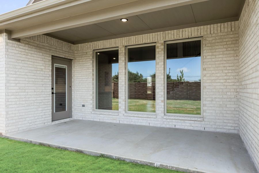 Covered back patio with concrete floor, white brick exterior, large windows, and back door leading inside.