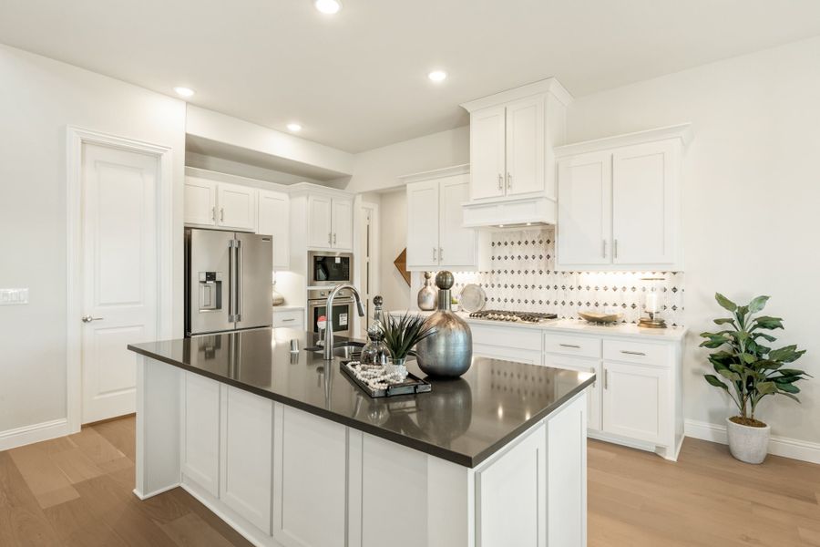 Kitchen with white cabinets, dark island countertop, patterned tile backsplash, and stainless steel appliances on light hardwood floors