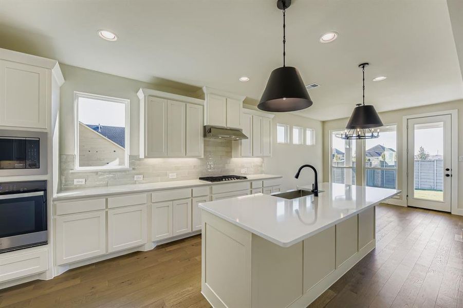 Kitchen featuring backsplash, stainless steel appliances, an island with sink, white cabinets, and recessed lighting