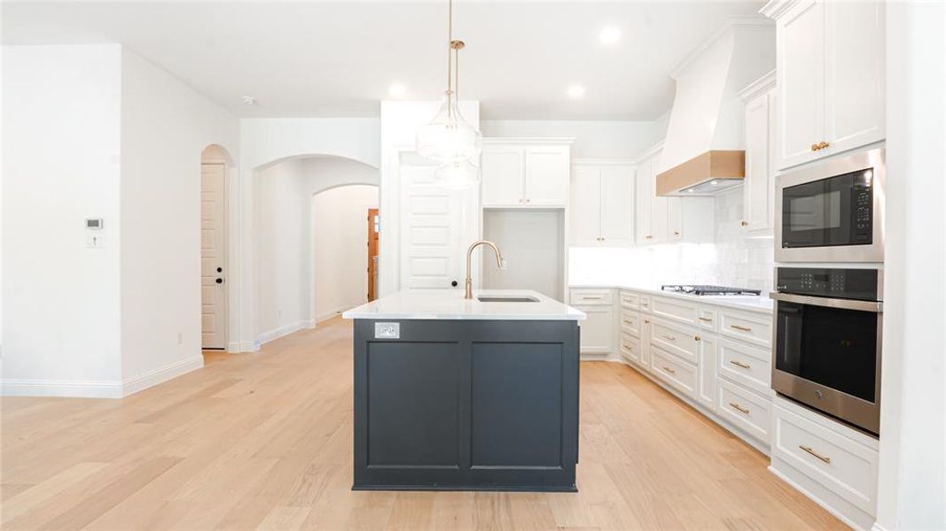 Kitchen featuring arched walkways, oven, light wood-style floors, built in microwave, and white cabinets Kitchen featuring arched walkways, oven, light wood-style floors, built in microwave, and white cabinets
