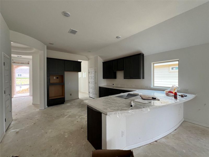 Kitchen featuring a peninsula, dark cabinetry, lofted ceiling, concrete flooring, and light countertops