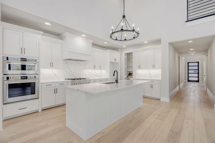 Kitchen with large island, white cabinets, stone counters, and modern light fixture