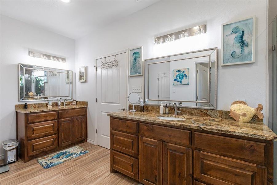 Dual vanity bathroom featuring wood-finish cabinetry, granite countertops, undermount sinks, and wood-finish flooring Dual vanity bathroom featuring wood-finish cabinetry, granite countertops, undermount sinks, and wood-finish flooring