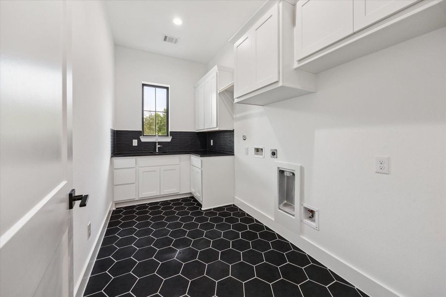 The utility room features bold black hex tile flooring, abundant cabinetry, a deep sink, and hanging space—blending practicality with sleek, modern design. A large window fills the space with natural light, making everyday tasks feel elevated. The utility room features bold black hex tile flooring, abundant cabinetry, a deep sink, and hanging space—blending practicality with sleek, modern design. A large window fills the space with natural light, making everyday tasks feel elevated.