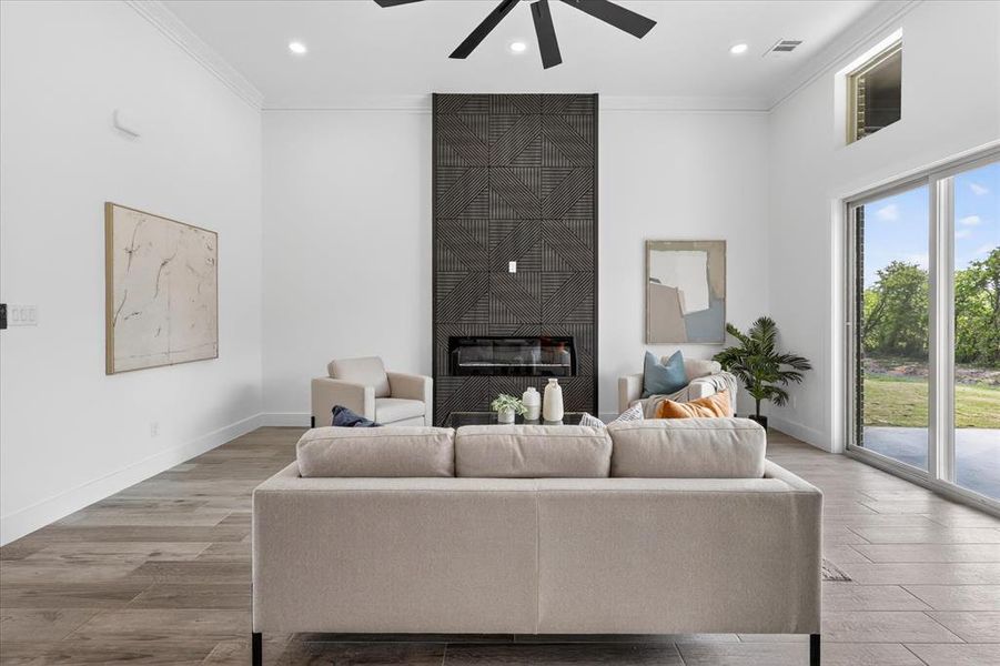 Living room with a large fireplace, light wood-style floors, crown molding, a high ceiling, and a ceiling fan