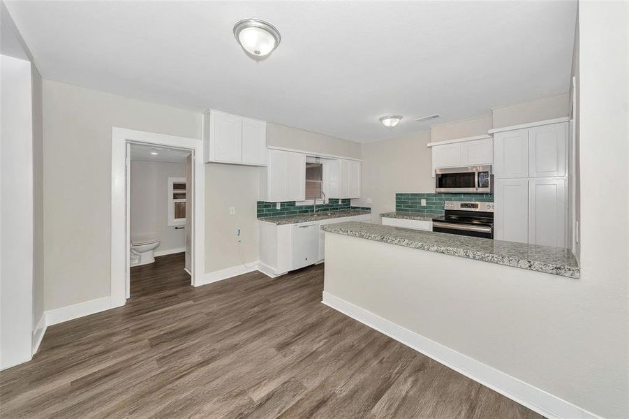 Kitchen with appliances with stainless steel finishes, white cabinetry, backsplash, dark wood-type flooring, and a peninsula Kitchen with appliances with stainless steel finishes, white cabinetry, backsplash, dark wood-type flooring, and a peninsula