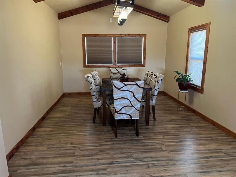 Dining space with vaulted ceiling with beams and dark hardwood / wood-style flooring