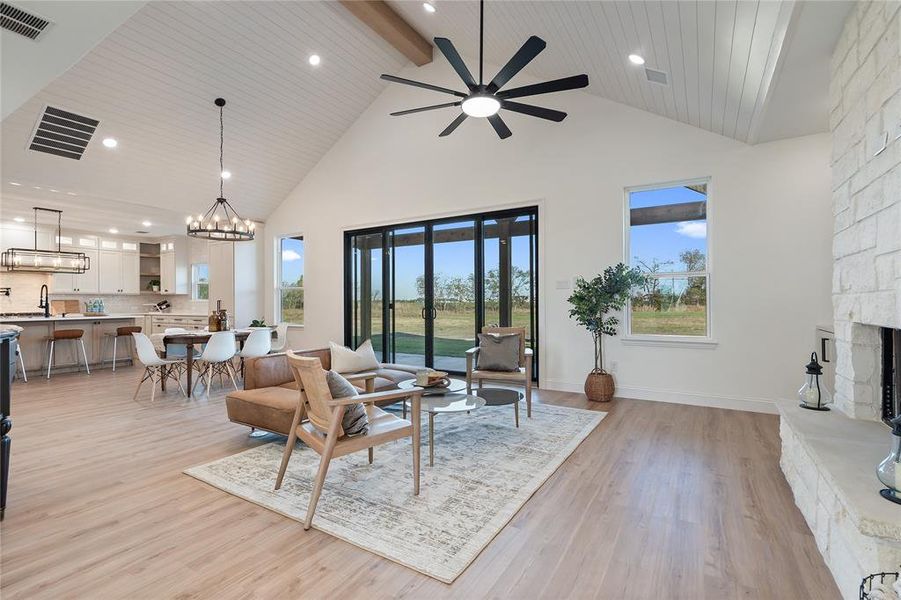 Living room with wood ceiling, ceiling fan with notable chandelier, light hardwood / wood-style flooring, high vaulted ceiling, and a stone fireplace