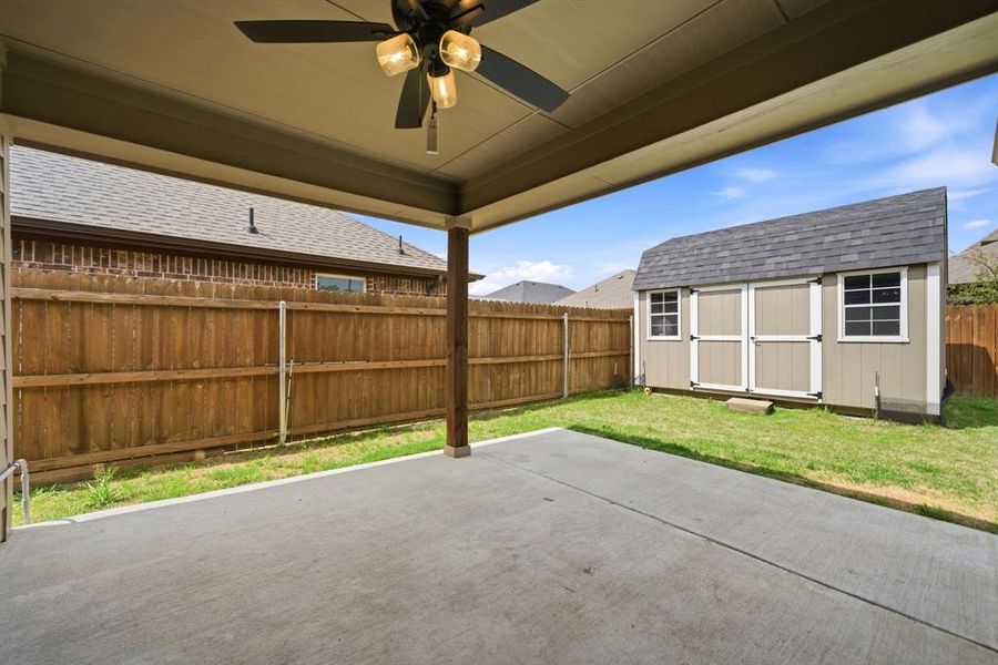 Fenced backyard featuring a ceiling fan, a patio, and a storage shed