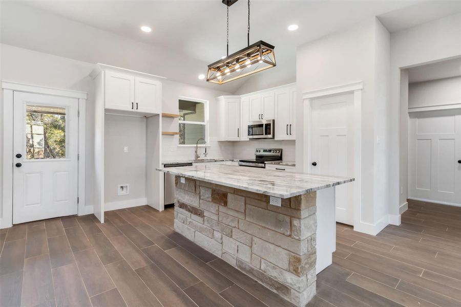 Kitchen with hanging light fixtures, stainless steel appliances, light stone countertops, white cabinets, and a kitchen island