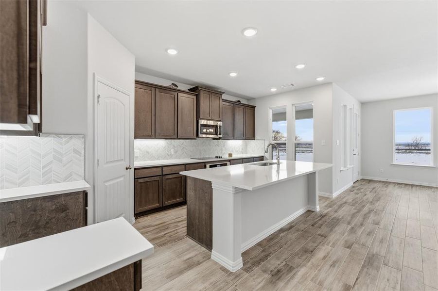 Kitchen featuring dark brown cabinetry, an island with sink, light wood-style flooring, tasteful backsplash, and recessed lighting Kitchen featuring dark brown cabinetry, an island with sink, light wood-style flooring, tasteful backsplash, and recessed lighting