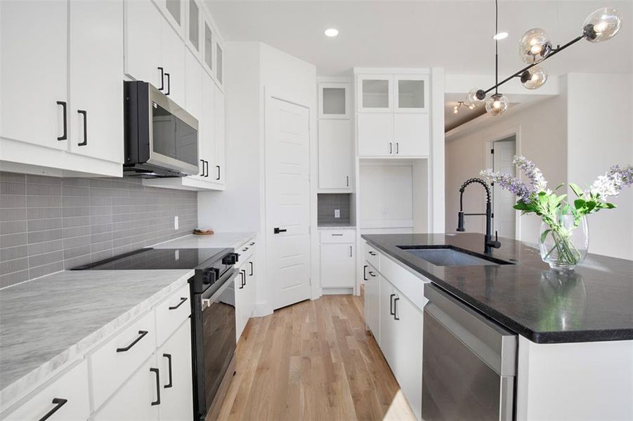 Kitchen with light wood-type flooring, stainless steel appliances, sink, a center island with sink, and white cabinets