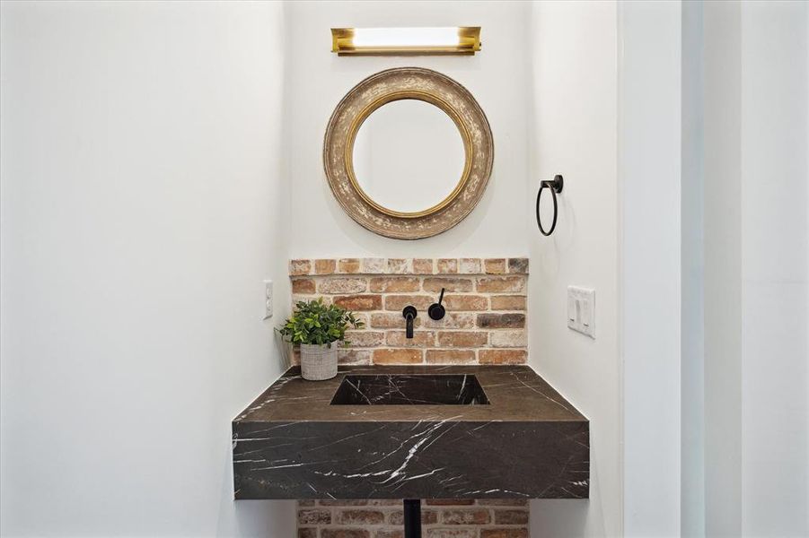 This powder room tucked behind the bookshelf features Visual Comfort vanity lighting, an integrated marble sink, and a matte black wall-mounted faucet, combining functionality with sophisticated design.