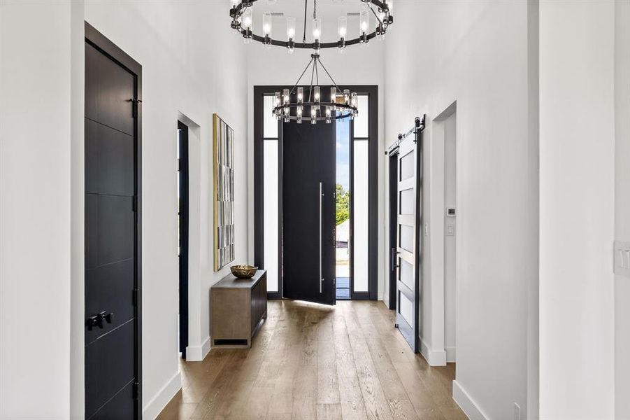 Entrance foyer with light wood finished floors, a high ceiling, a barn door, and a chandelier