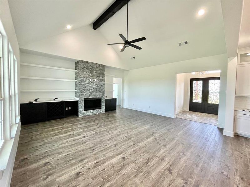 Unfurnished living room featuring light wood-type flooring, visible vents, beamed ceiling, ceiling fan, and high vaulted ceiling Unfurnished living room featuring light wood-type flooring, visible vents, beamed ceiling, ceiling fan, and high vaulted ceiling