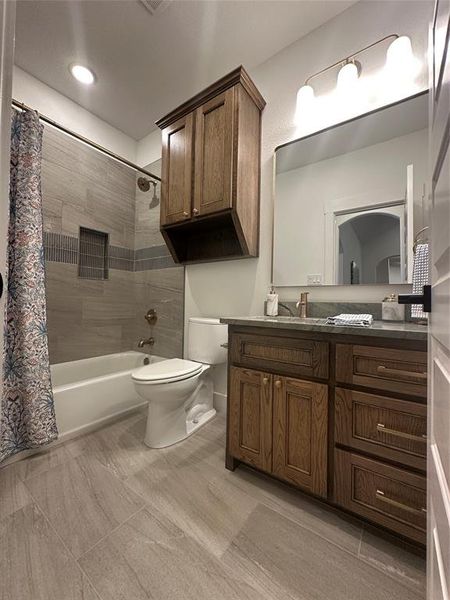 Bathroom featuring wood-finish vanity with countertop, large mirror, and three-light fixture