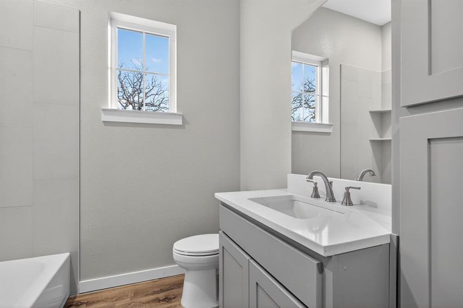 Light and bright secondary bathroom has tub/shower combo with custom tile work, vanity, and cabinet storage.