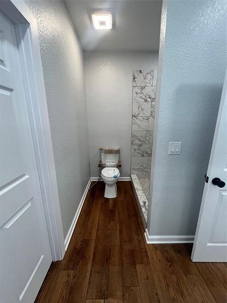 Bathroom with a textured wall, dark wood-style floors, and a stall shower Bathroom with a textured wall, dark wood-style floors, and a stall shower