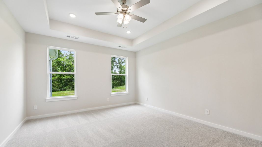 Primary Bedroom with tray ceiling, carpet, and ceiling fan
