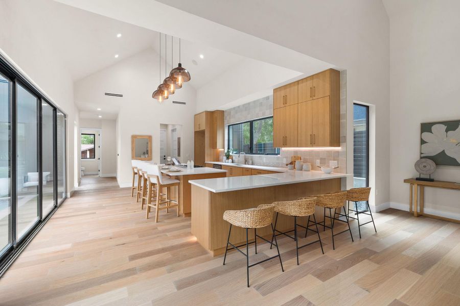 Vaulted ceilings accent an open-concept kitchen and living area featuring light wood-finish flooring