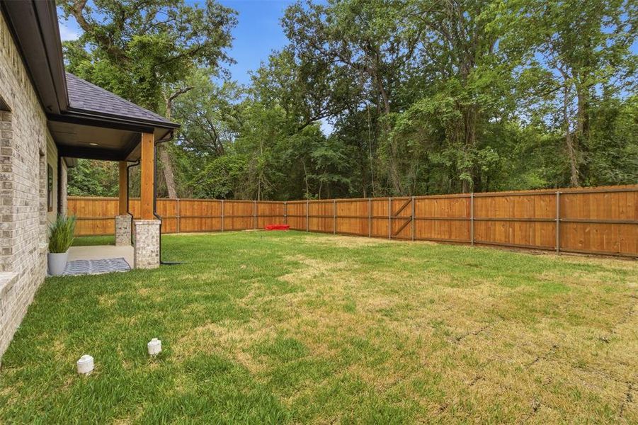 Expansive backyard featuring a new wood privacy fence, a covered patio with brick and wood columns, and ample green space