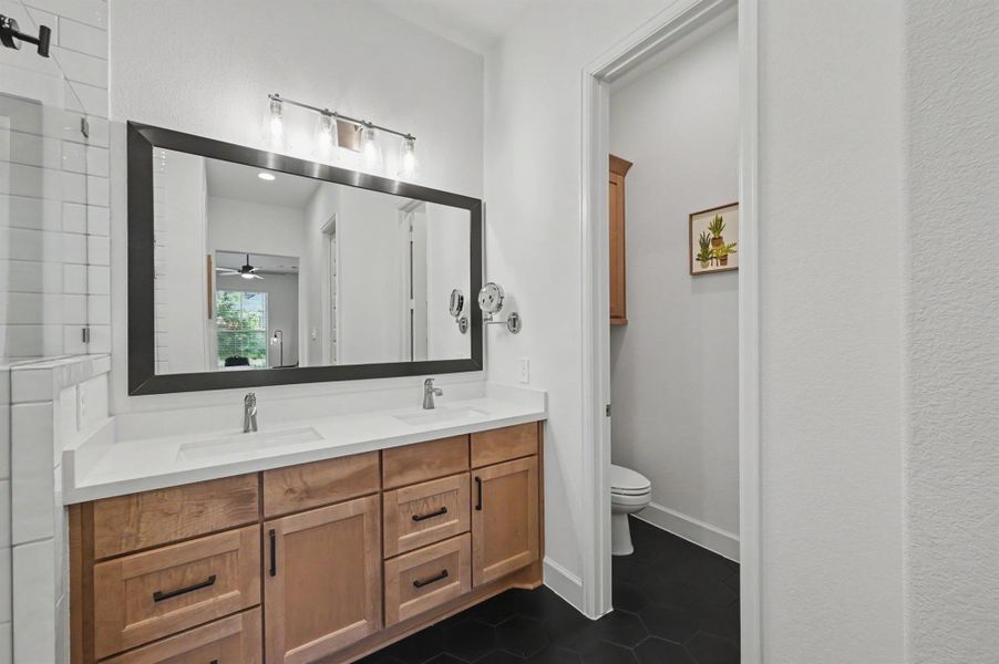 There are two undermount sinks with brushed nickel faucets in the vanity along an upgraded quartz countertop. The mirror is framed and the light fixture is an upgrade. A maple stained cabinet was added in the toilet area. There are two undermount sinks with brushed nickel faucets in the vanity along an upgraded quartz countertop. The mirror is framed and the light fixture is an upgrade. A maple stained cabinet was added in the toilet area.