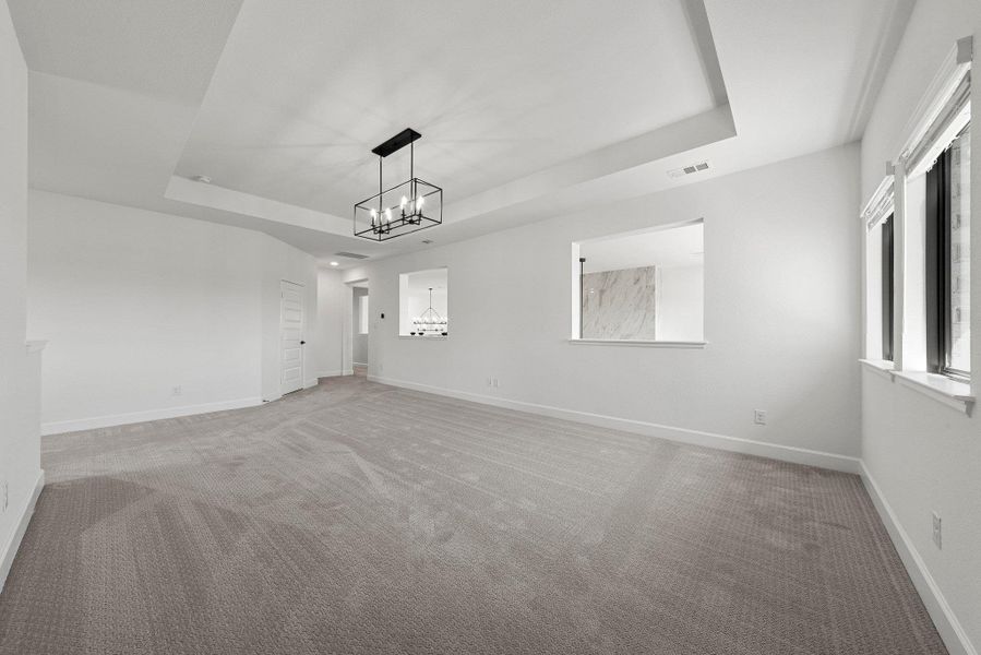 Empty room featuring light carpet, visible vents, baseboards, a tray ceiling, and a notable chandelier