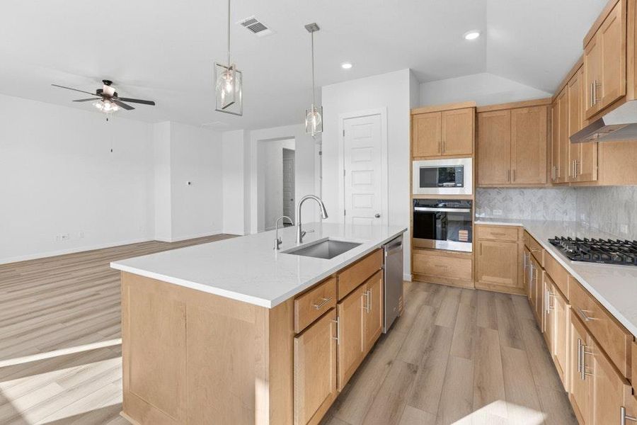 Kitchen featuring light wood-style floors, tasteful backsplash, hanging light fixtures, a center island with sink, and stainless steel appliances