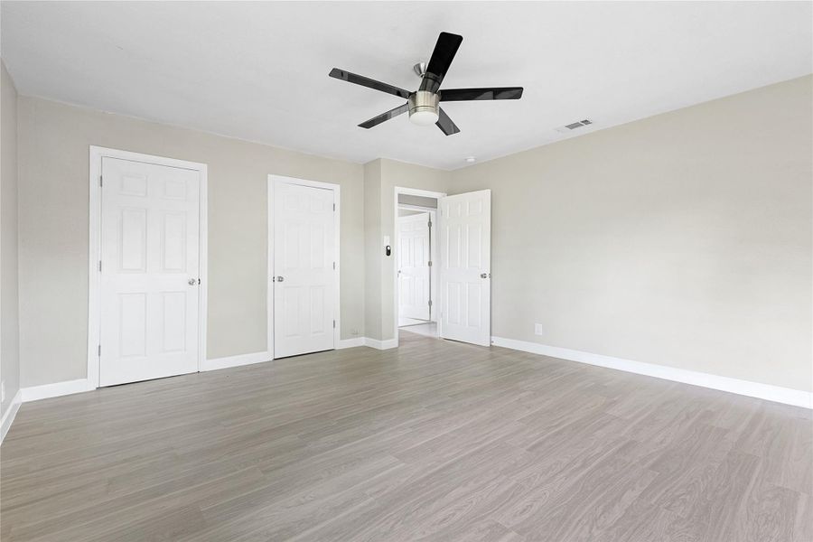 This spacious room features light wood flooring, neutral walls, a modern ceiling fan, and multiple doors for access and storage. Ideal for a bedroom or office.