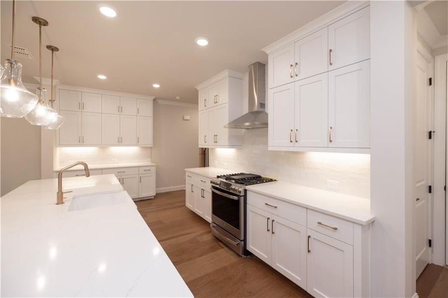 Kitchen with stainless steel gas range oven, white cabinets, wall chimney range hood, decorative light fixtures, and backsplash