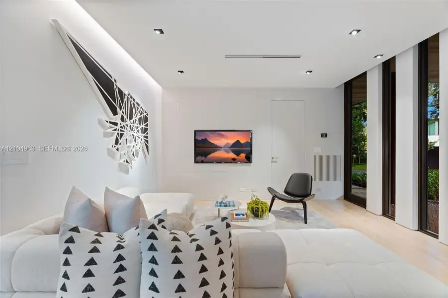 Contemporary interior featuring smooth wall panels, light-toned wood-finish flooring, recessed ceiling lighting, and floor-to-ceiling windows with dark frames