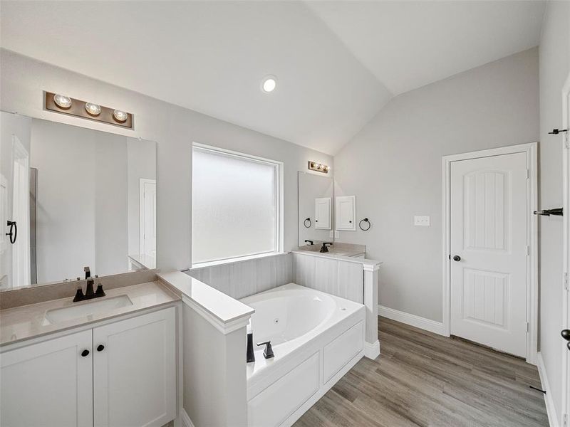 Full bath featuring a garden tub, vaulted ceiling, two vanities, wood finished floors, and a sink