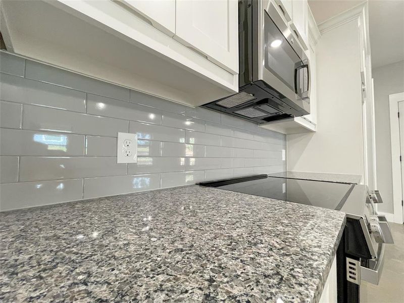 Kitchen with appliances with stainless steel finishes, stone counters, white cabinets, and decorative backsplash