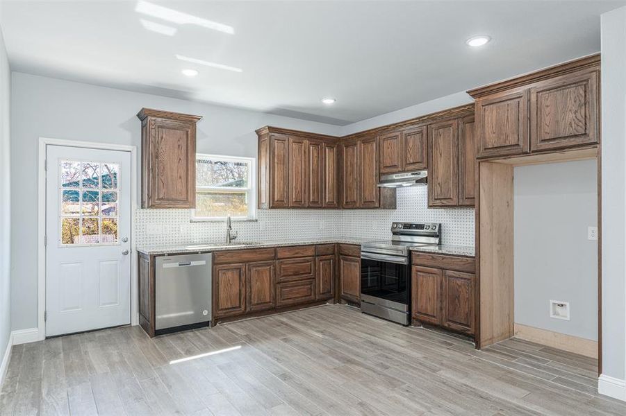 Kitchen featuring under cabinet range hood, light stone counters, stainless steel appliances, and light wood-style floors