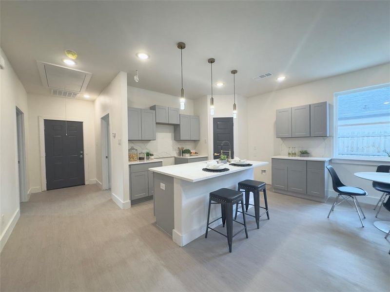 Kitchen with light hardwood / wood-style floors, gray cabinets, backsplash, and a kitchen island with sink